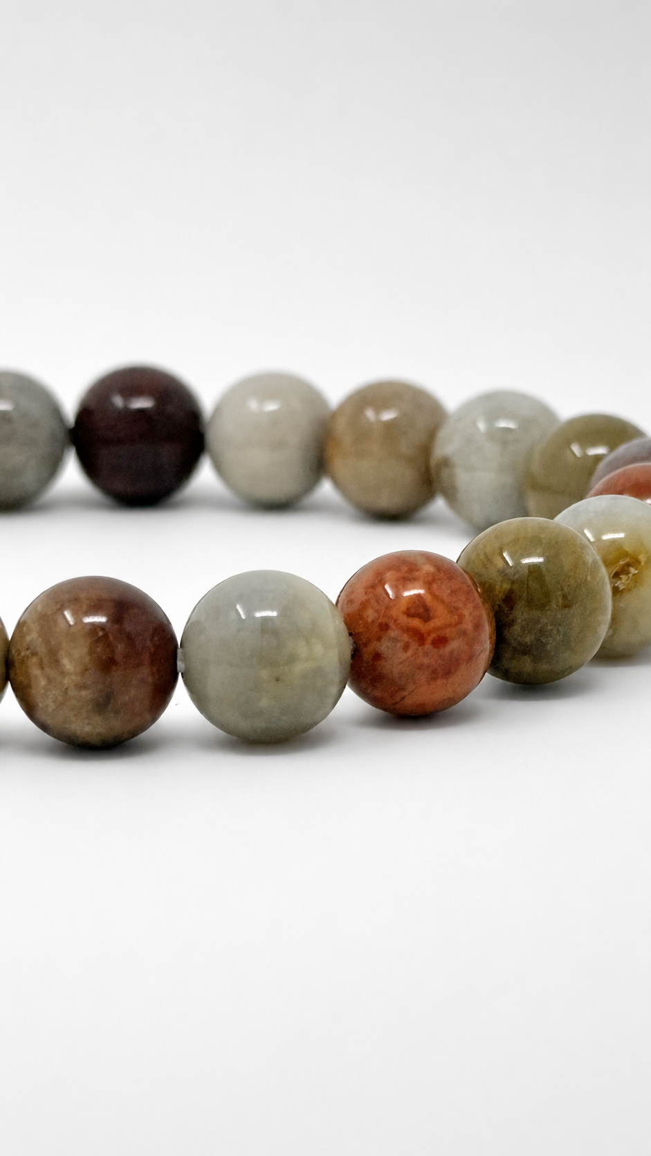 A strand of polished round gemstone beads in assorted earthy colors, including brown, gray, green, orange, and cream, arranged in two curved rows on a white background.